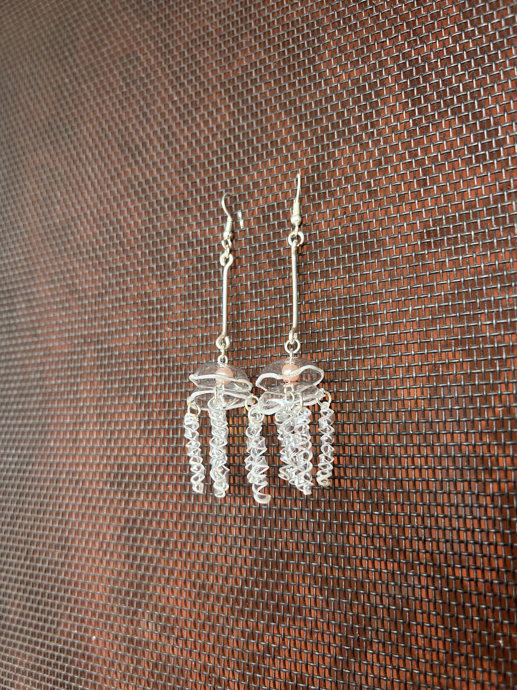 Clear jellyfish earrings hanging against a textured screen.